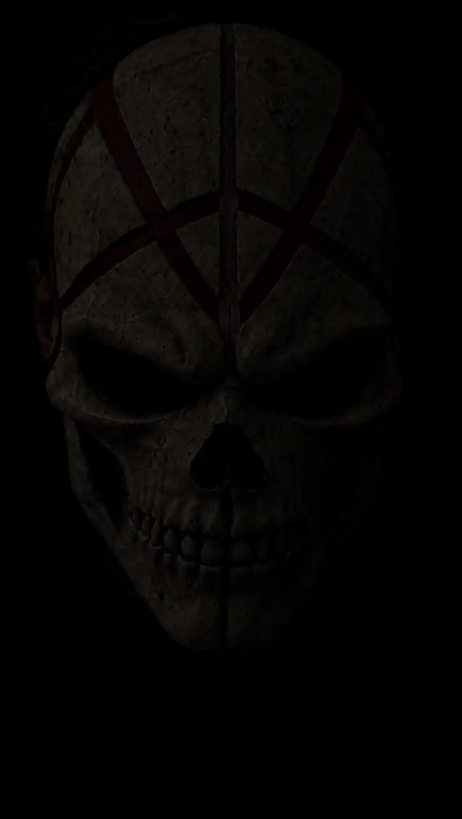 A man in a skull mask marked with red, still, in the dark.